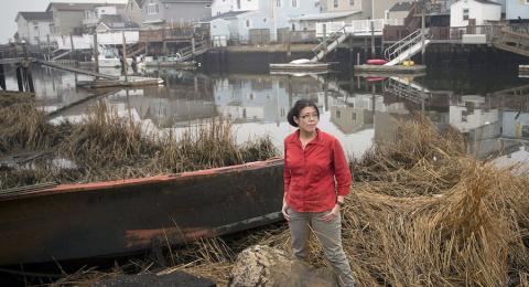 Helen standing by the shore with row of houses in background.