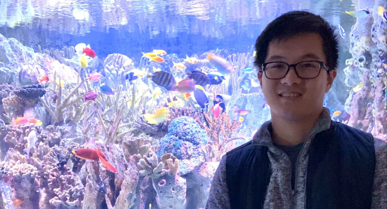 Photo of James standing in front of a colorful fishtank. 