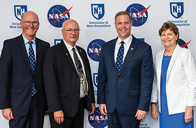 Photo of Harlan Spence, Jeanne Shaheen and NASA crew in front of NASA backdrop. 