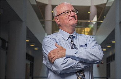 Photo of Harlan Spence in Morse Hall smiling with arms crossed. 