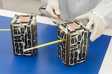 Two NASA cubesats being worked on by researcher in white gloves.