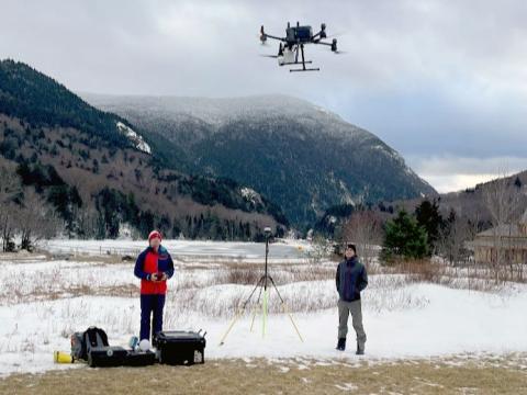 Photo of two people flying a drone with snow covered mountains in background.