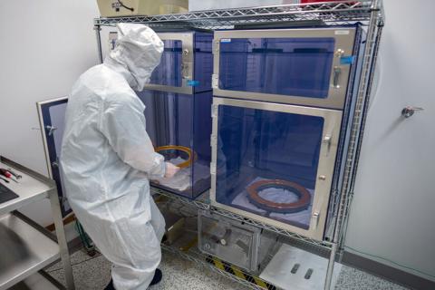 Photo of researcher in a white suit removing a disk from a glass cabinet.