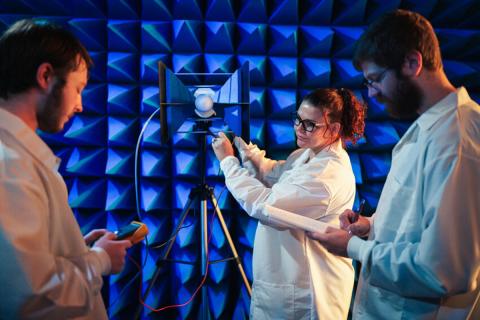 Photo of three researchers looking at a device inside a blue spikey chamber.