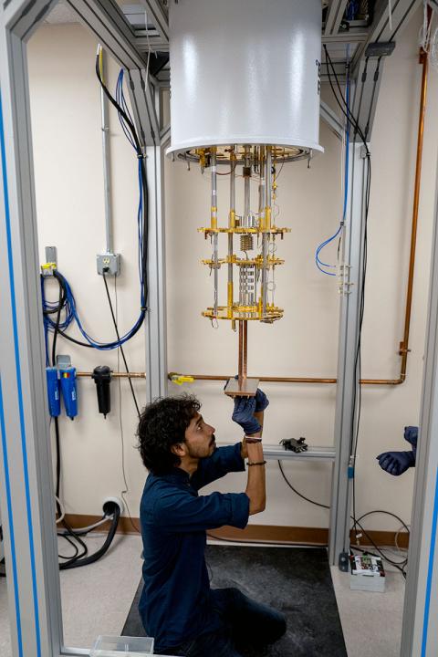 Color photo of man working on dilution fridge in lab. 
