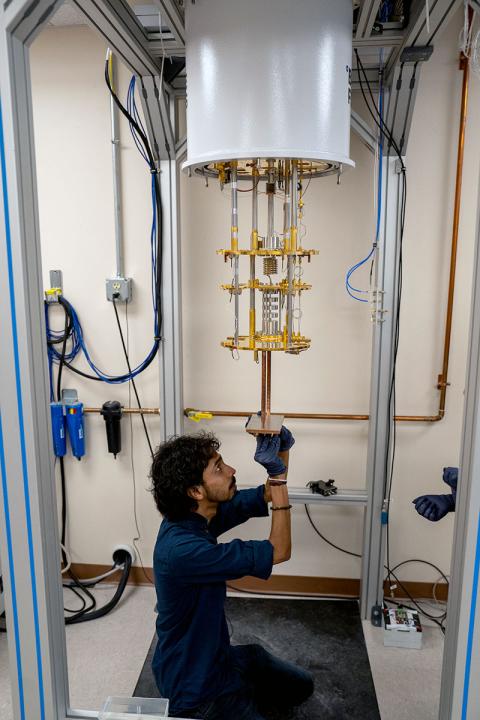 Color photo of man working on dilution fridge in lab.