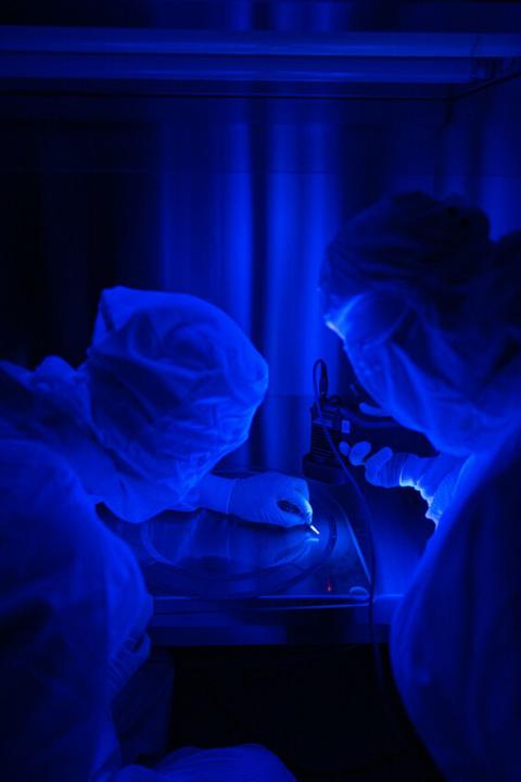 Two people in lab working on instrument under blue light.