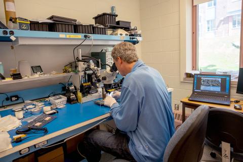 Color photo of man looking through microscope in Assembly Lab. 