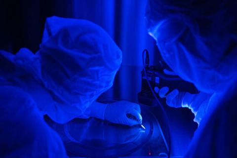 Blue image of two researchers working on an instrument.