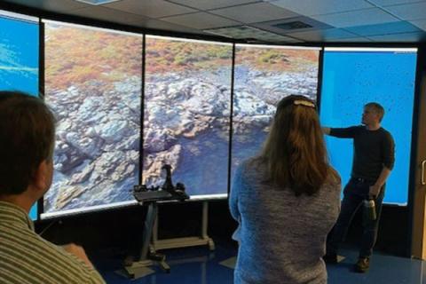 Photo of man pointing to the VisLab screen with two onlookers in the room. 