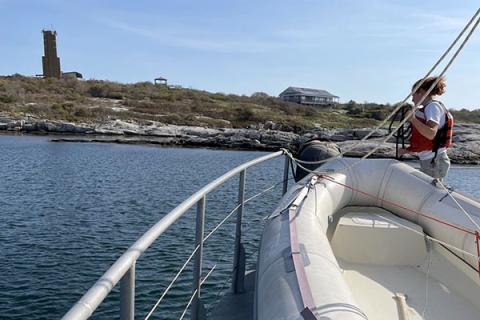 Image of person on front of boat with land in background.