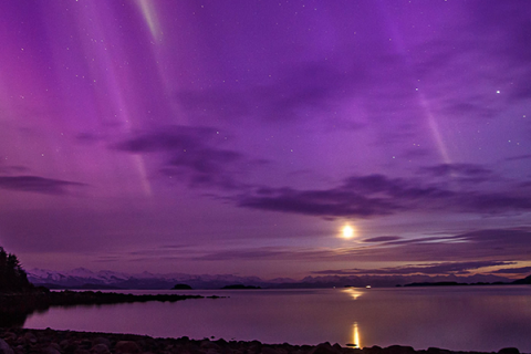 Photo of sunset over water with purple aurora borealis in sky. 