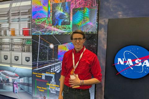Photo of man standing in front of app graphics and NASA sign. 