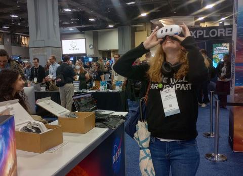 Woman with VR goggles at trade show looking up and smiling. 