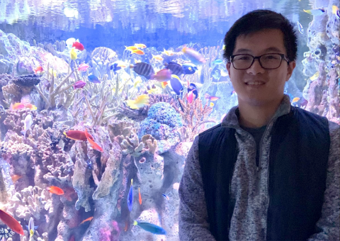 Photo of James standing in front of a colorful fishtank. 
