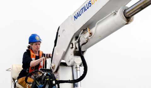 Erin Heffron operating a large crane aboard the Exploration Vessel (E/V) Nautilus. Erin operating a large crane on the ocean.