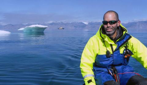 Tomer Ketter on expedition through the Northwest Passage, Canadian Arctic. Testing out a small zodiac inflatable boat with mothership Icebreaker Oden in the background. Tomer seated in front of ocean and icebergs.
