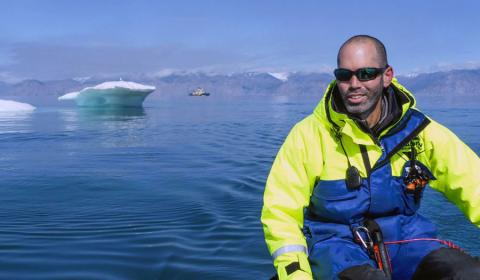 Tomer seated in front of ocean and icebergs.